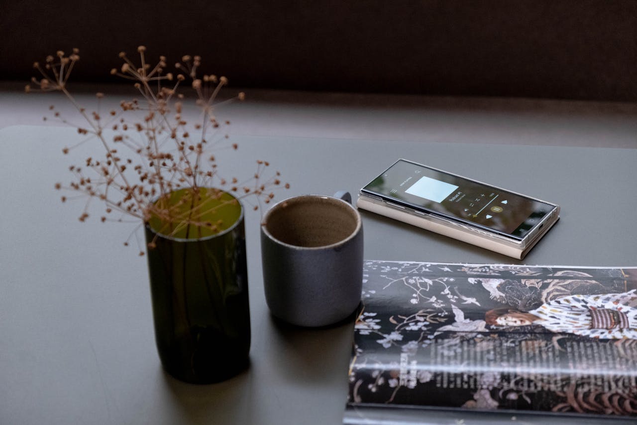 who-we-are A stylish table setting featuring dried flowers, a smartphone, and a fashion magazine.